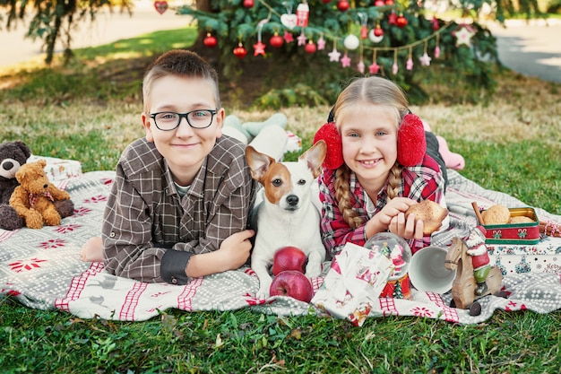 Niños niño y niña con un perro jack russell terrier cerca de un árbol de navidad con regalos,