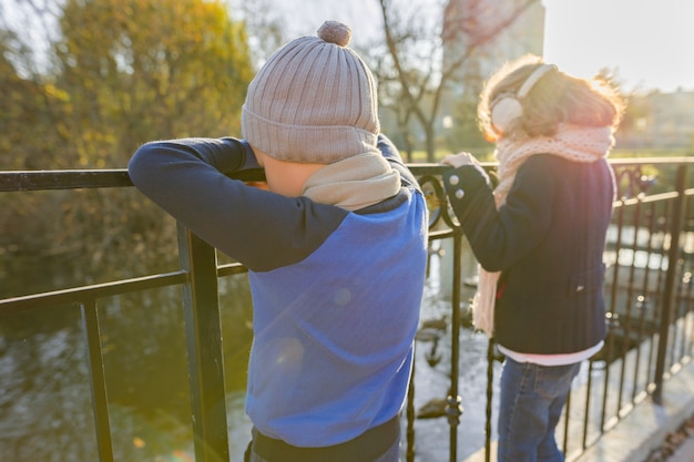 Niños niño y niña de pie de espaldas en el puente, mirando patos