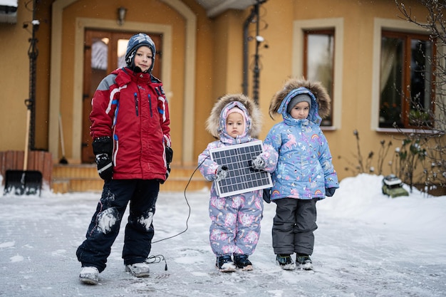 Niños con panel solar contra casa en invierno Concepto de energía alternativa