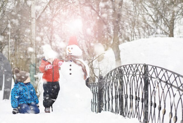 Niños en el parque en invierno. Los niños juegan con nieve en el patio de recreo. Esculpen muñecos de nieve y se deslizan por las colinas.