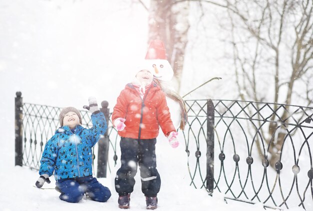 Niños en el parque en invierno. Los niños juegan con nieve en el patio de recreo. Esculpen muñecos de nieve y se deslizan por las colinas.