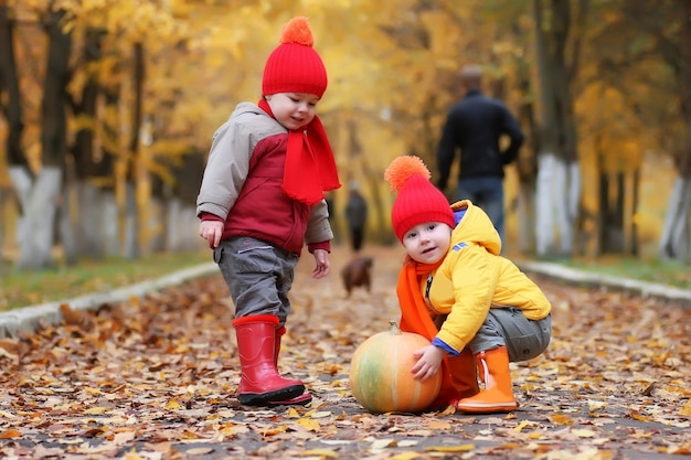 Niños en el parque de otoño con calabaza alrededor de hojas de otoño