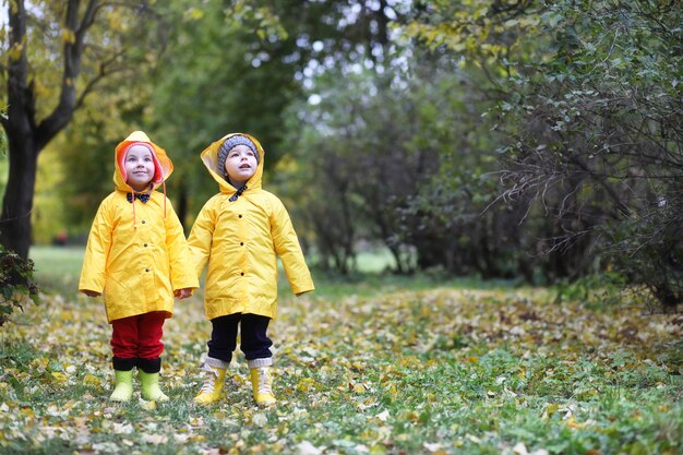 Los niños en el parque de otoño caminan con impermeables durante el día.