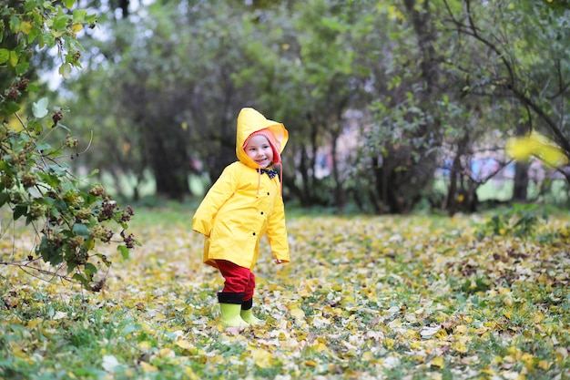 Los niños en el parque de otoño caminan con impermeables durante el día.