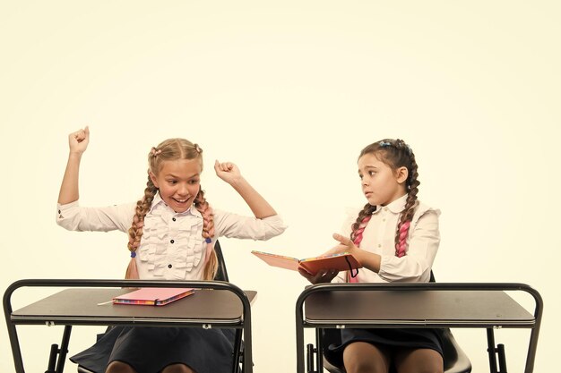 Los niños pequeños aprenden a leer y escribir en la escuela Habilidades de lectura Impresión opuesta La actitud personal determina el éxito Adquirir conocimientos Las niñas pequeñas con libros se sientan en los escritorios leyendo la lección