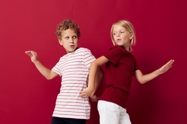 Niños pequeños de buen humor parados junto a un fondo rojo posando