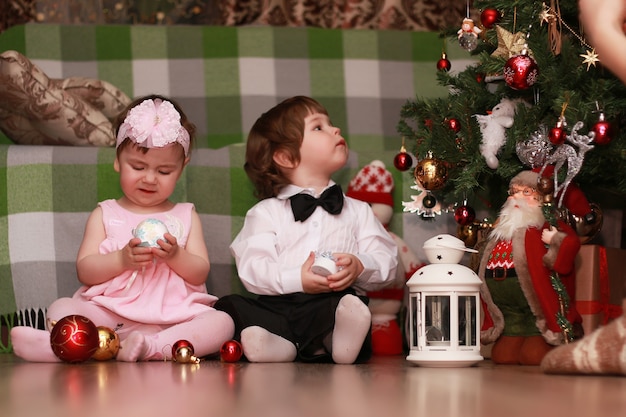 Los niños pequeños cerca de un árbol de Navidad antes de las vacaciones.