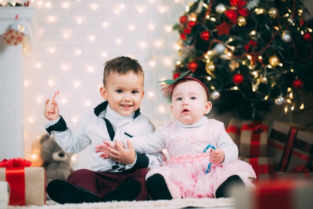 Los niños pequeños cerca del árbol de Navidad y la chimenea con caramelos de colores en sus manos