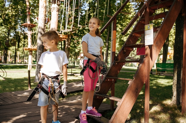 Niños pequeños en equipo, parque de cuerdas, parque infantil. Niños subiendo en puente colgante.