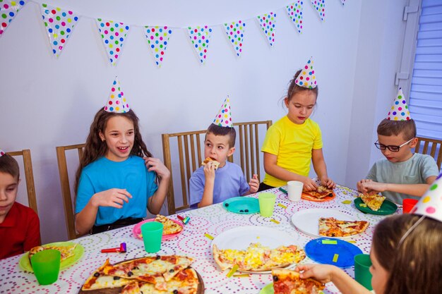 Los niños pequeños están comiendo pizza en la fiesta de cumpleaños.