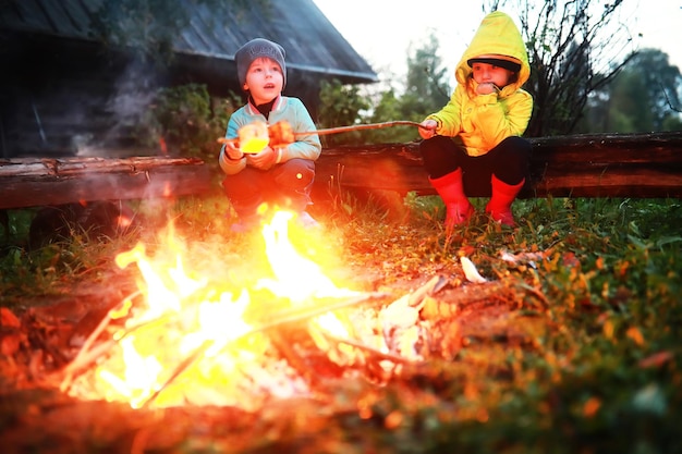 Niños pequeños friendo malvaviscos en la noche de la hoguera. Campamento de verano