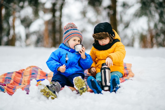 Foto los niños pequeños hacen un picnic en el bosque de invierno. jóvenes bebiendo té de termo en bosque nevado.