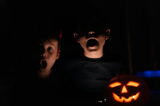 Foto niños pequeños haciendo caras aterradoras en la oscuridad a la luz del concepto de halloween jackolantern