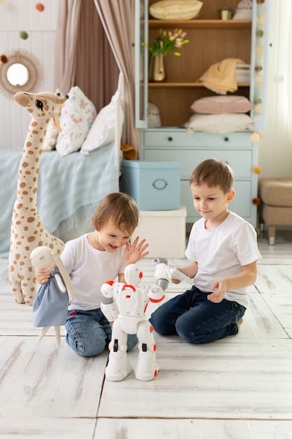 Los niños pequeños, hermano y hermana, se sientan en el suelo de la habitación, riendo y jugando con el robot.