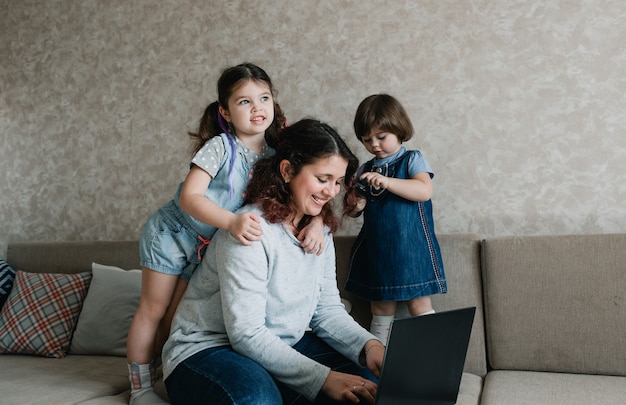 Los niños pequeños impiden que su madre trabaje en la computadora. trabajo remoto en casa