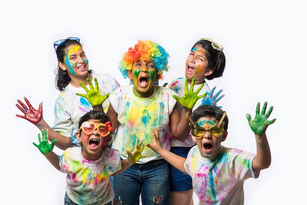 Niños pequeños indios o amigos o hermanos celebrando el festival de Holi con gulal o color en polvo, dulces, pichkari o spray, aislado sobre fondo blanco.