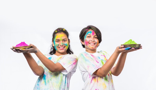 Niños pequeños indios o amigos o hermanos celebrando el festival de Holi con gulal o color en polvo, dulces, pichkari o spray, aislado sobre fondo blanco.