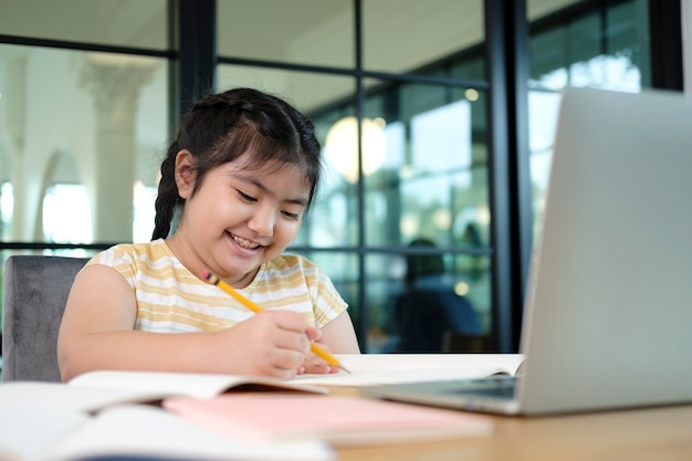 Niños pequeños lindos y felices que usan la computadora portátil, estudiando a través del sistema de e-learning en línea.