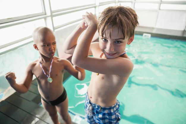 Niños pequeños de pie junto a la piscina con medallas