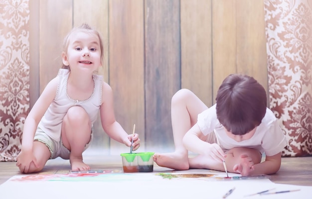 Los niños pequeños pintan en una hoja grande de papel en el suelo