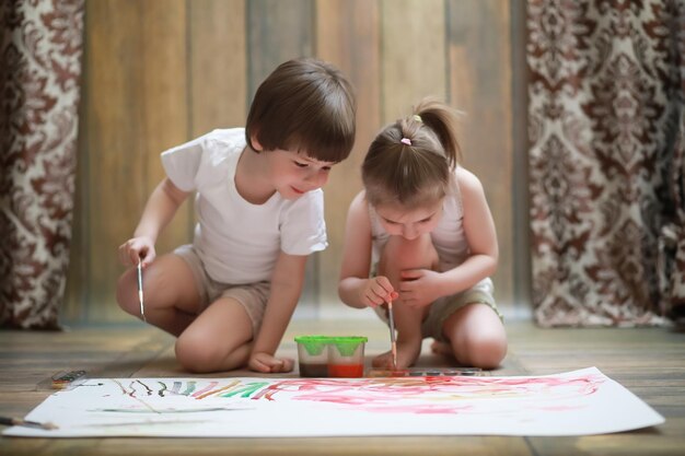 Los niños pequeños pintan en una hoja grande de papel