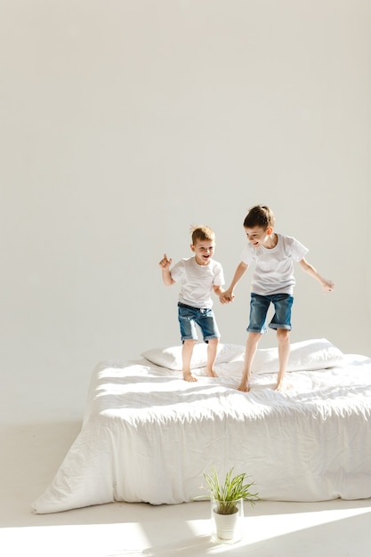 Niños pequeños saltando sobre una cama y divirtiéndose bajo el sol.