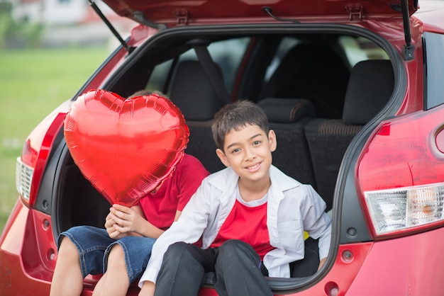 Niños pequeños sentados en la puerta trasera del auto con globo en la mano