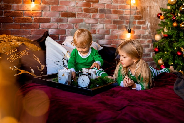 niños en pijama con cacao cerca del árbol de Navidad