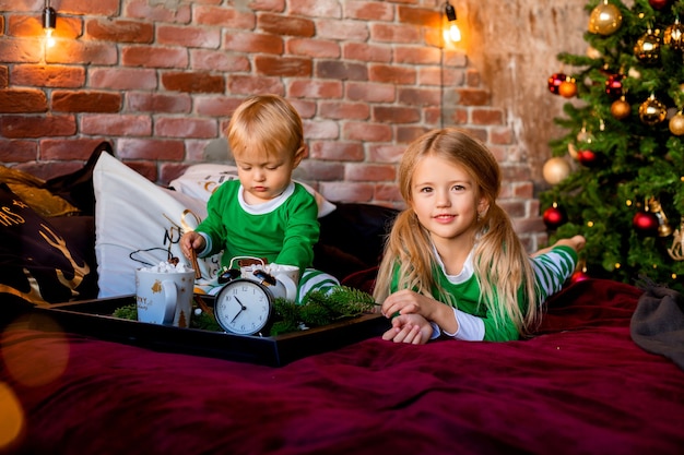 niños en pijama con cacao cerca del árbol de Navidad