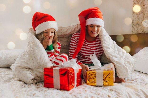 Niños en pijama y gorros navideños en la cama con regalos. concepto de navidad y año nuevo