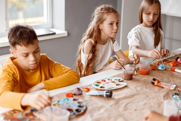 Niños pintando sobre papel con pinturas de colores en la escuela.