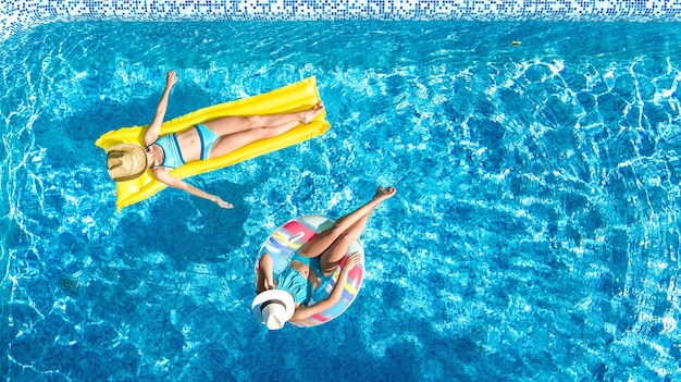 Los niños en la piscina vista aérea del dron desde arriba, los niños felices nadan en un anillo inflable y un colchón, las niñas activas se divierten en el agua durante las vacaciones familiares en el centro vacacional