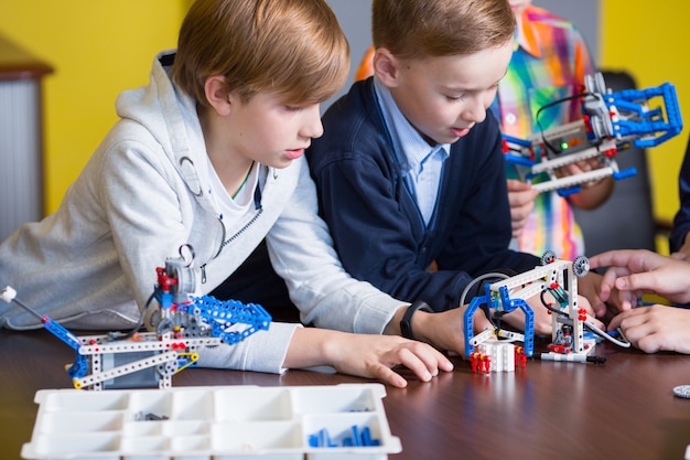 Los niños positivos juegan y ensamblan al constructor en la habitación de los niños.