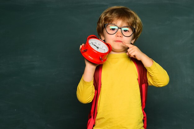 Los niños se preparan para la escuela. El niño pequeño lindo apaga el despertador y se despierta por la mañana ...