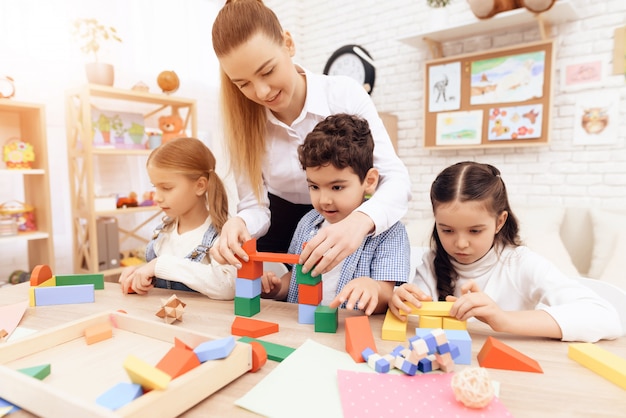 Los niños que juegan con cubos de madera y la maestra les está ayudando.