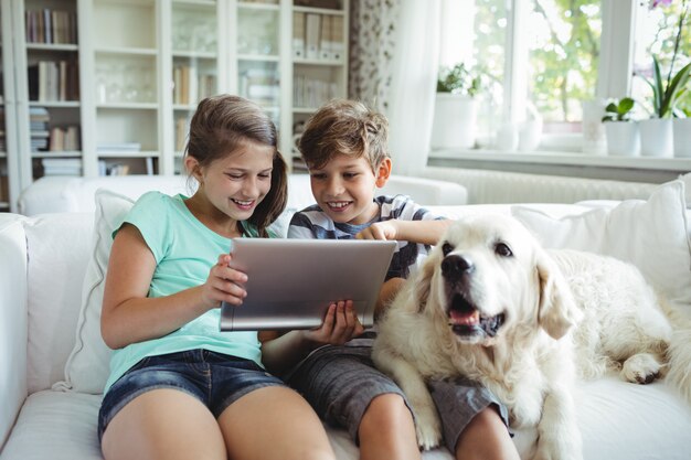 Niños que usan tableta digital mientras están sentados en un sofá