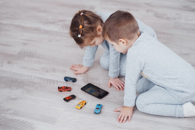 Niños que utilizan dispositivos digitales en casa. Hermano y hermana en pijama ven dibujos animados y juegan juegos en su tableta tecnológica.