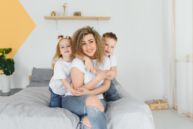 Niños riendo jugando con su madre acostada en una cama en casa