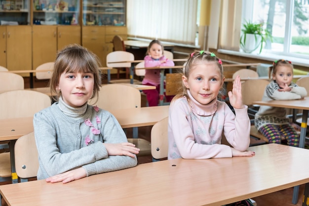 Los niños en el salón de clases se sientan en los escritorios y un estudiante levanta la mano.