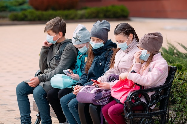 Los niños de Schoolage en máscaras médicas se sientan en un banco