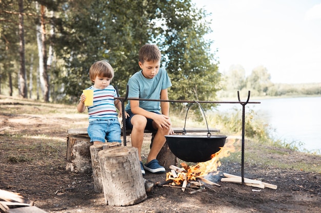 Niños sentados alrededor de una fogata en el bosque en verano Picnic familiar al aire libre Vida de camping Cocinar en caldero en llamas en la naturaleza