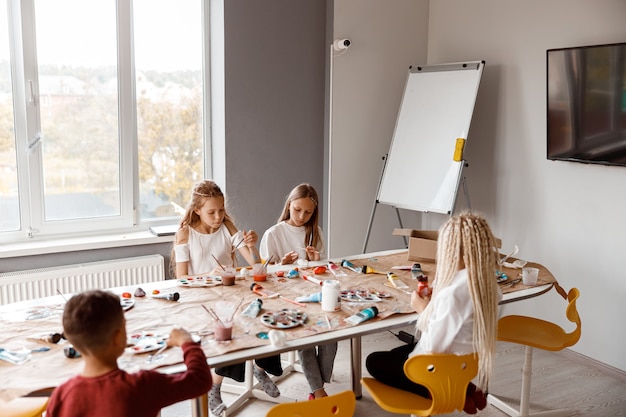 Niños sentados a la mesa y dibujando con entusiasmo con acuarelas sobre papel