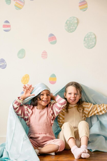 Niños sentados en el piso de madera mientras se esconden debajo de la manta Foto de stock