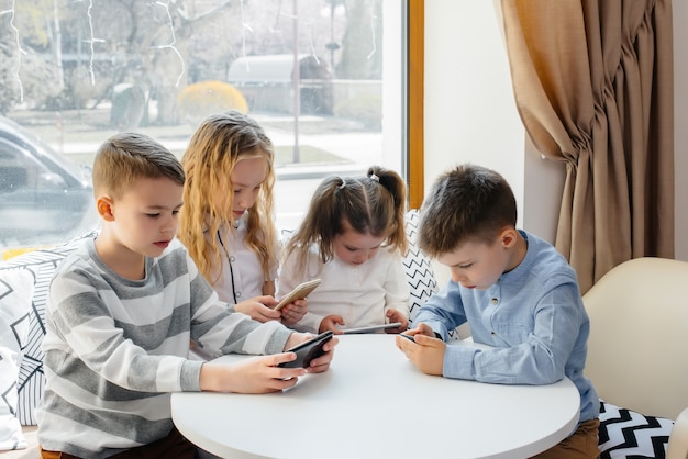 Los niños se sientan en una mesa en un café y juegan juntos teléfonos móviles. Entretenimiento moderno
