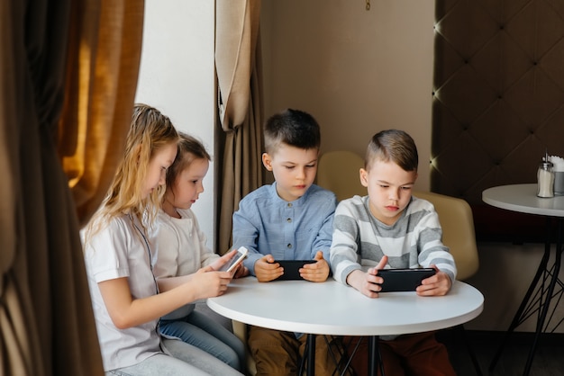 Los niños se sientan en una mesa en un café y juegan juntos teléfonos móviles. Entretenimiento moderno