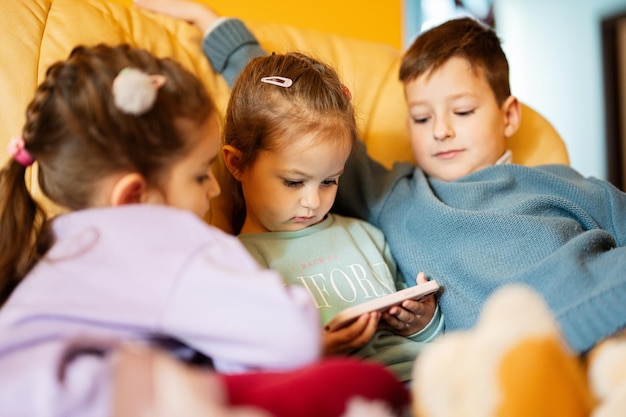 Los niños se sientan en un sofá de cuero en la sala de estar y miran dibujos animados por teléfono