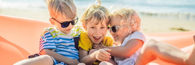 Los niños se sientan en un sofá inflable contra el mar y se divierten con un cartel de formato largo