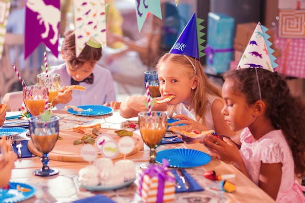 Niños con sombreros de fiesta y disfrutando de la comida.