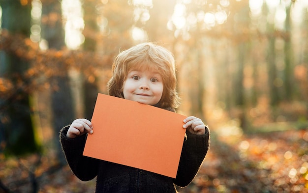 Los niños sonrientes del otoño sostienen una hoja en blanco para el espacio de texto Publicidad y venta Niño sosteniendo publicidad