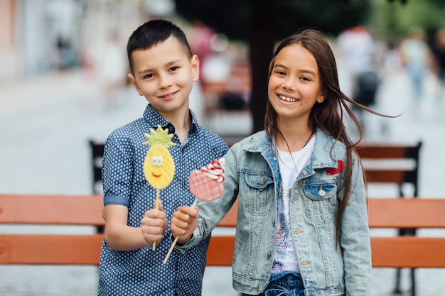 Foto niños sonrientes con piruletas, cerca del banco de madera en el parque